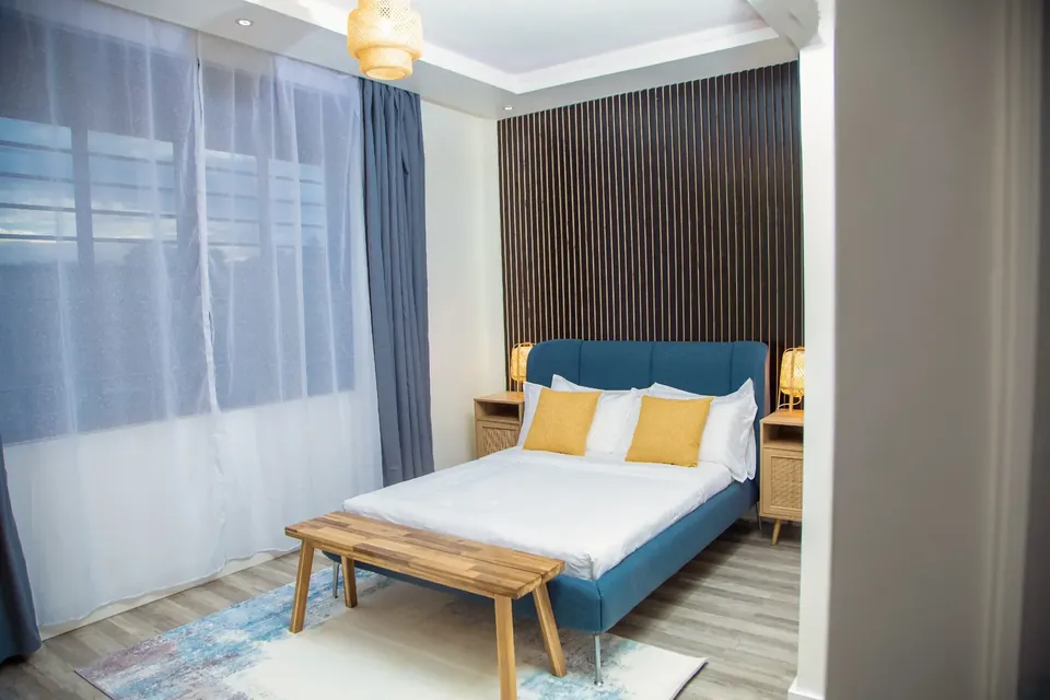 Bedroom with blue upholstered double bed, wooden bench and rattan bedside lamps