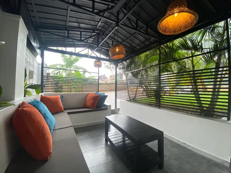 Shaded terrace seating with rattan pendant lights overlooking the garden at Behomu Apartments