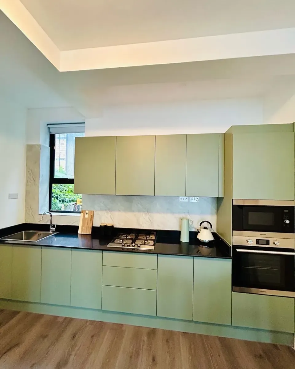 Sage-green kitchen cabinets with black countertop and gas hob
